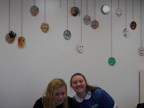 Two Junior Humanities students, Annie Maras and Carolyn Rutishauser, pose with masks made by the phase four class.