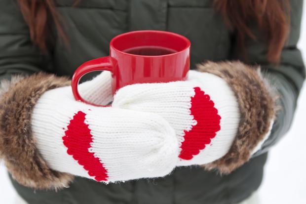 Hands in mittens with hearts holding cup